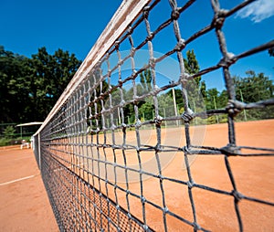 Tennis net on red clay court with lines and shadows.