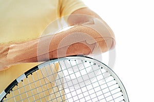 Tennis player elbow taped with elastic therapeutic or Kinesio tape applied on arm lying on racket at orthopedic ward close up