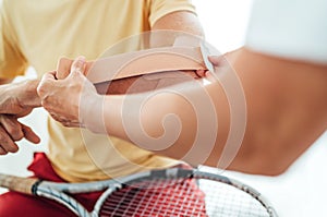 Tennis player elbow taped with elastic therapeutic or Kinesio tape applied by nurse at orthopedic ward close up image. Active