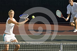 Tennis Player Hitting Ball With Partner Standing In Background