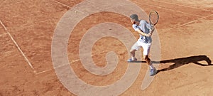 Tennis player playing on clay court. Young male tennis player hitting backhand hit. Sports banner. Copy space for text