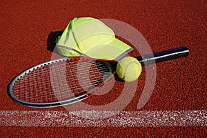 Tennis racket, peaked cap and balls on court