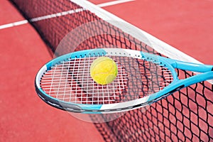 On the tennis racket lies a yellow tennis ball against the background of the court.