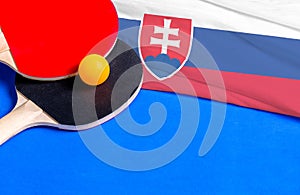 Tenisové rakety a míček s vlajkou Slovensko na modrém pozadí, maketa vlajky. Koncept soutěže stolního tenisu