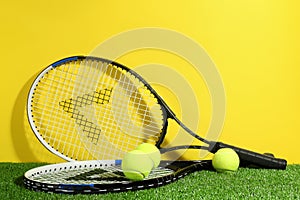 Tennis rackets and balls on green grass against yellow background. Sports equipment