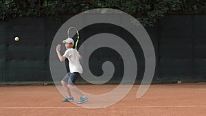 Tennis sportsmanship, ambitious child boy concentrating and focusing on game and racket beats ball on red court