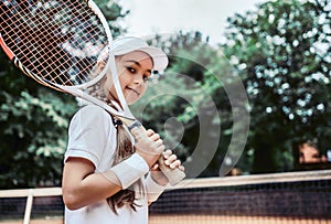 Tennis training for young kid outdoors. Portrait of happy sporty little girl on tennis court. Caucasian child in white tennis