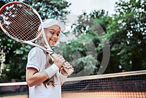 Tennis training for young kid outdoors. Portrait of happy sporty little girl on tennis court. Caucasian child in white tennis