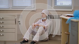 A tense, exhausted a female doctor sits tiredly on the hospital floor