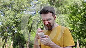 Tense man with crossed fingers holding smartphone and showing yeah gesture