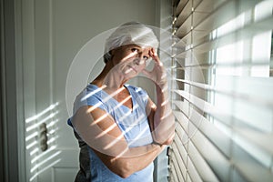 Tense senior woman standing near window in bedroom