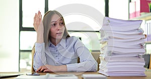 Tense young business woman sitting at table with computer stocking paper documents