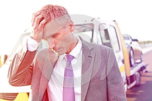 Tensed businessman standing against tow truck on road