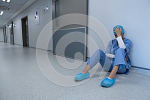 Tensed female surgeon sitting in the corridor of hospital