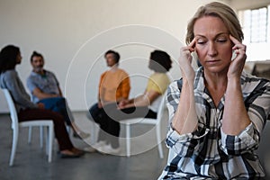 Tensed woman with head in hand while friends discussing in background