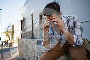 Tensed young man with head in hands sitting on retaining wall