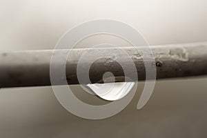 Tensioned wire after rain with a drop of water from below in the focus of composition with depth of field. Gray art background