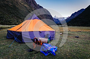 tent, bottles and backpacks in base camp with high snowy mountains in the background, on the trekking of the quebrada santa cruz