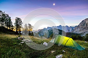 A tent glows under a moon night sky at twilight hour. Alps, Triglav National Park, Slovenia.