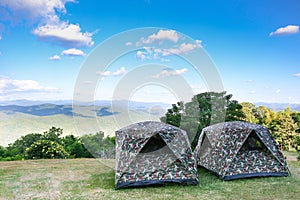 Tent on the hill beneath the mountains under clear sky in beautiful summer landscape camp. The camouflage tent is on green fields