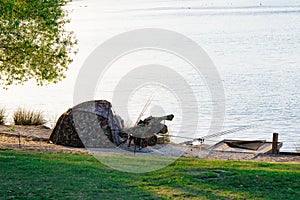 Tent near lakeshore at sunset and carp fishing technique rod in freshwater