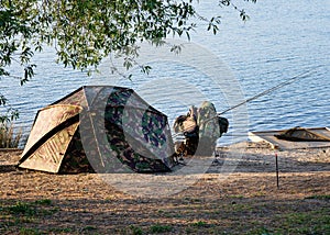 Tent near lakeshore at sunset and carp fishing technique rod in freshwater