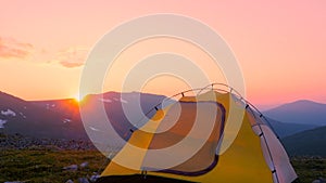 The tent stands against the background of the setting sun and the mountain range. Camp of tourists on the pass at sunset. Hiking