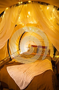 Tent with very cozy bed, blankets, pillows and lights, at a glamping