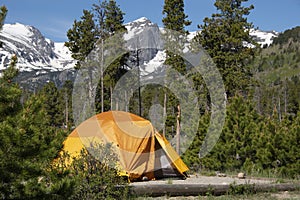 Tenting in Orange tent camping with Hallet Peak and snow covered Rocky Mountains of Colorado