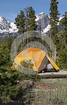 Tenting in orange tent camping with Hallet Peak and snow covered Rocky Mountains of Colorado
