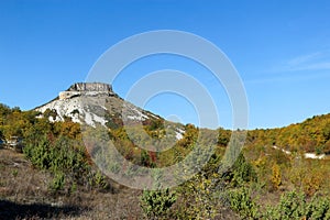 Tepe Kermen Cave City near Bakhchysarai in Crimea surrounded by colorful autumn forest under bright blue sky