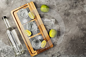 Tequila bottle and shots, limes, salt on wooden board. Top view, copy space