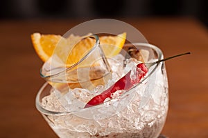 tequila in a glass on a pillow of crushed ice in a bowl, served with chili, orange and caramelized sugar. close-up