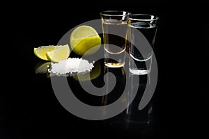 Tequila gold and silver in glasses, lime and salt. On a black background