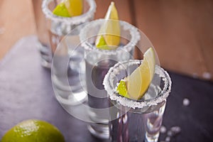 Tequila shot with lime and sea salt on black tray, selective focus