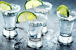 Tequila shot with lime slices and salt on dark background