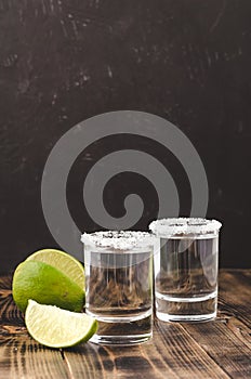 Tequila shot with lime slices and salt on wooden table/Tequila shots and lime slice on wooden table.With copy space on black