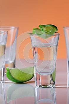 Tequila shot with a slice of lime on the glass orange background