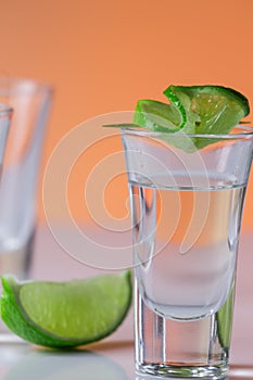 Tequila shot with a slice of lime on the glass orange background