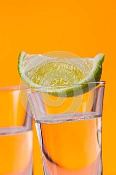 Tequila shot with a slice of lime on the glass orange background