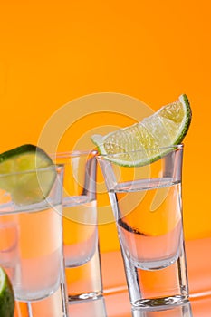 Tequila shot with a slice of lime on the glass orange background