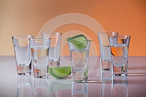 Tequila shot with a slice of lime on the glass orange background