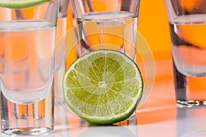 Tequila shot with a slice of lime on the glass orange background