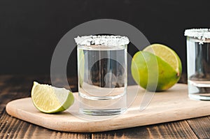 Tequila shots with lime slices and salt on wooden support /Tequila shots and lime slice on wooden table