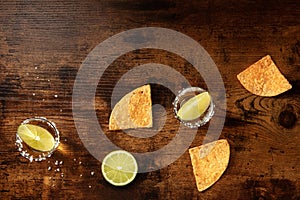 Tequila shots with salty rims, lime slices, and nacho chips,