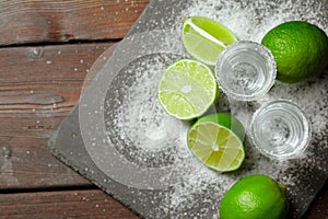 Tequila silver shots with lime slices and salt on wooden board