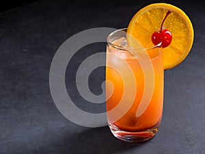 Tequila sunrise cocktail on dark stone background with copy space.