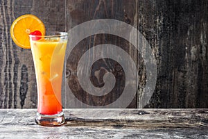 Tequila sunrise cocktail in glass on wooden table.