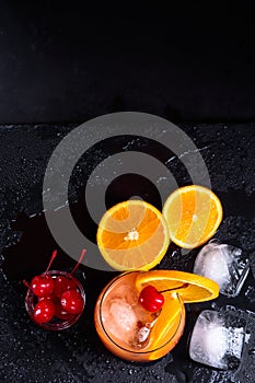 Tequila Sunrise cocktail, orange, ice cubes and maraschino cherries on a wet black slate tray. Top view with copy space.