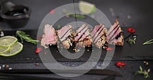 Teriyaki or soy sauce pours onto Sliced grilled fried tuna steak covered with sesame seeds on a black stone serving